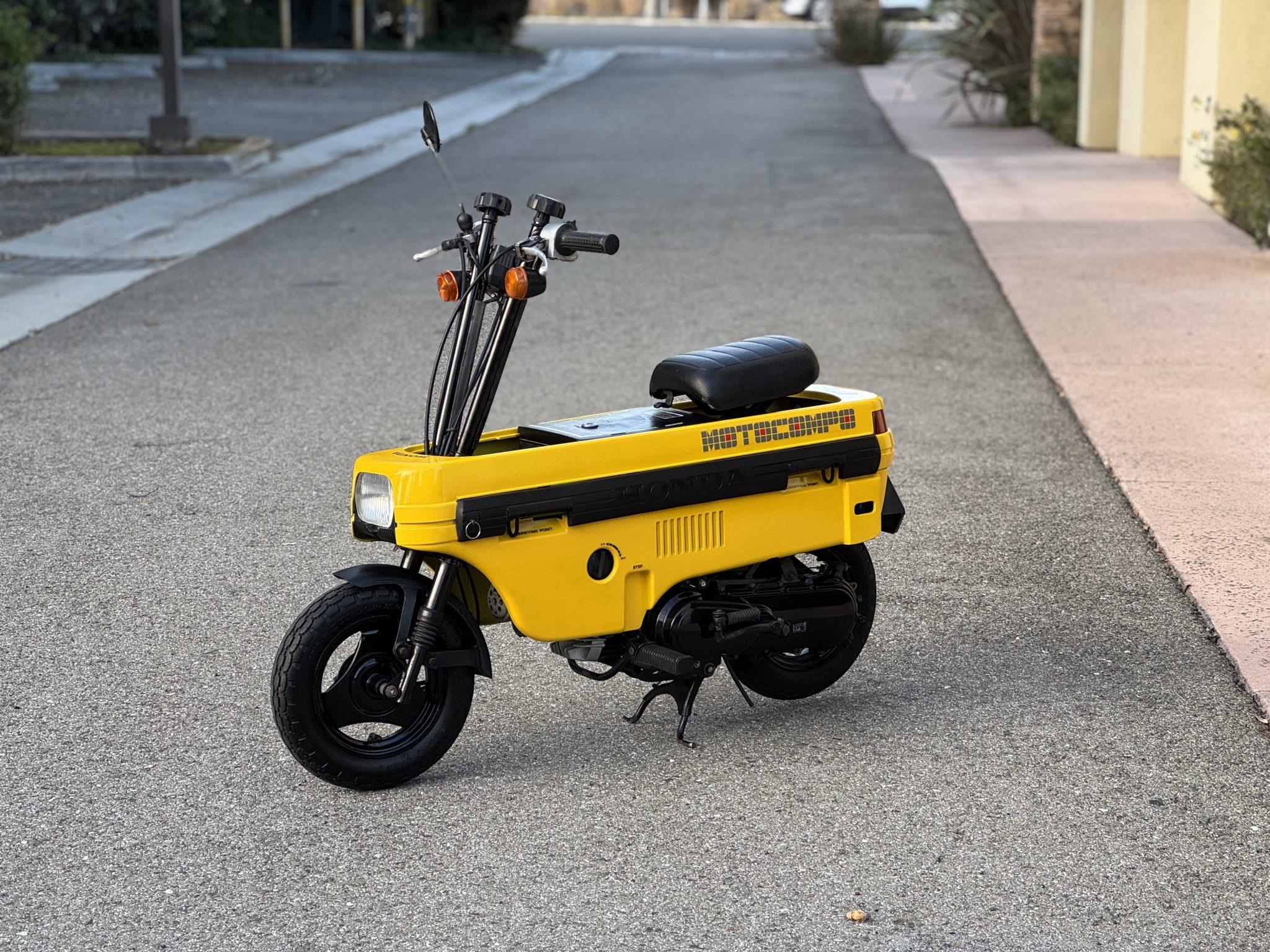 This 1982 Honda Motocompo is finished in yellow and is powered by an air-cooled 49cc two-stroke single linked to a single-speed transmission with an automatic clutch. Features include a black vinyl pop-up seat and handlebars that fold flat as well as oil injection, a kick starter, a center stand, street lighting, 8″ three-spoke steel wheels, drum brakes, full suspension, and integrated lift/tie-down points for transport.