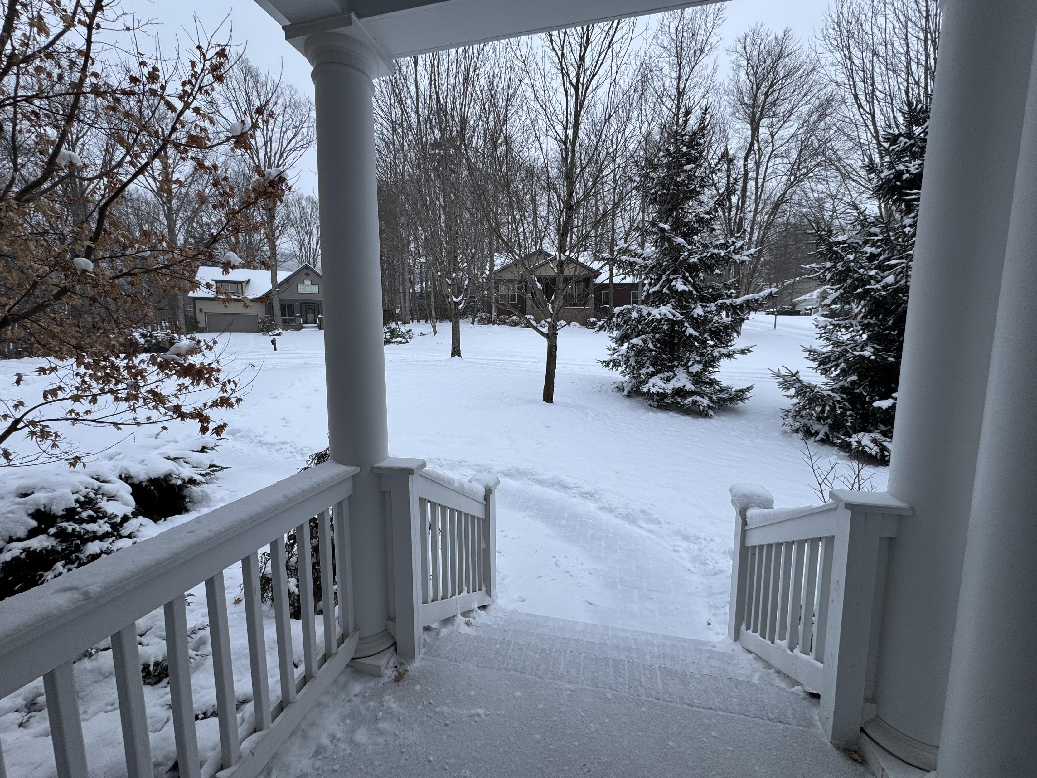 It has settled a bit but I imagine this is 4-5" of beautiful powdery snow.  

Taken from my front porch, one can see the snow has covered part of the porch again, along with the stairs and a pathway along the right side of the pavers that I had shoveled and then swept.  The other side, and the driveway was only shoveled.

The scene is still tranquil, with very light snow falling, two houses visible across the court, and a variety of trees partially covered in powder.  We have not seen blue skies or the sun today at all.  I believe all of that will change tonight... ok, we won't see blue skies or sun tonight either, but you know what I mean.