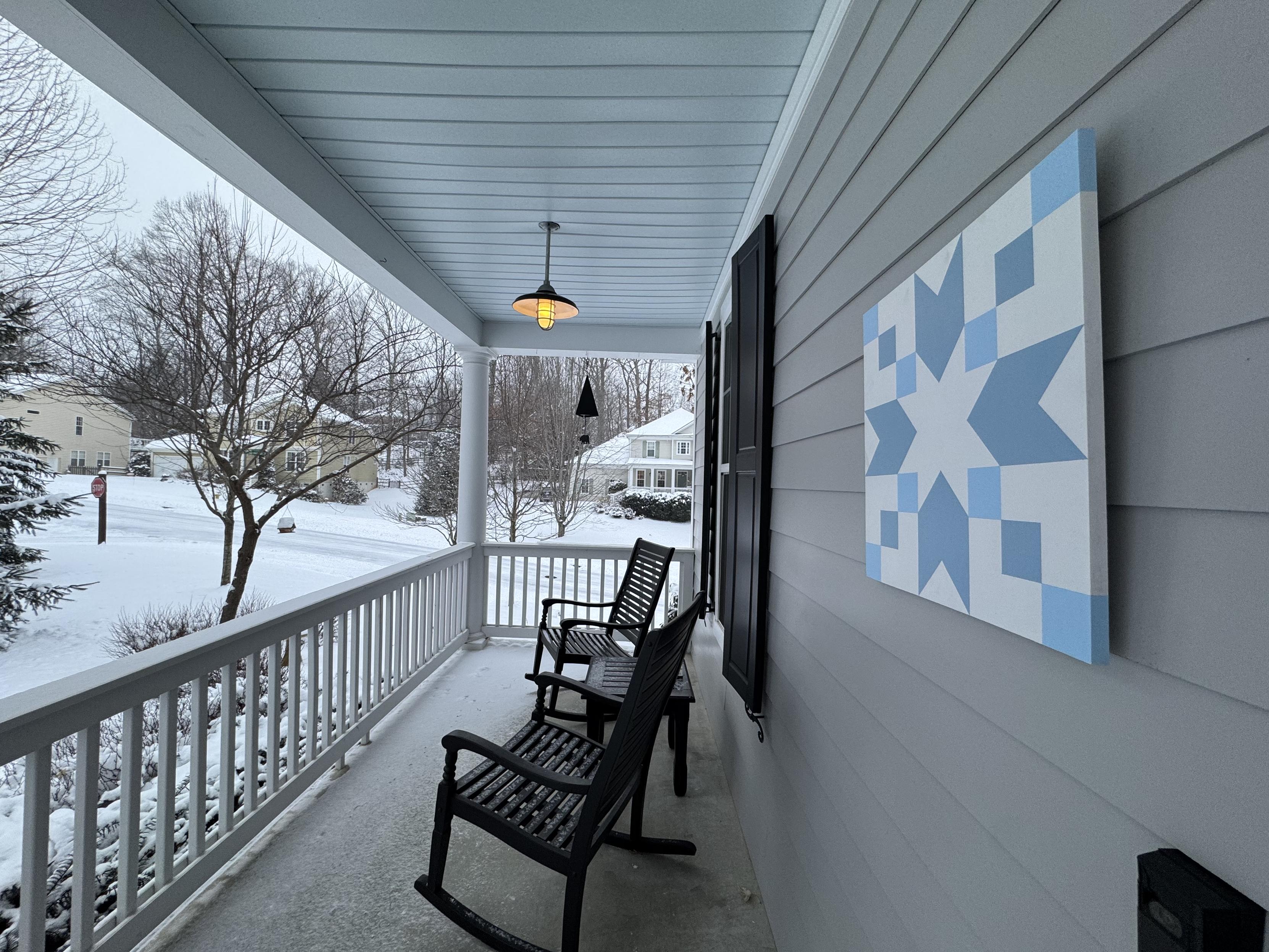 Looking to the right across the porch, one sees a pair of black rocking chairs and a table, a hanging barn light, a bear bell, and then a lot of snow and other houses across a hill of a street.  This is one of the streets that the non-AWD cars attempted and then from which they retreated.

Hanging on the wall of the house is a light blue and white quilt square in the pattern of a snowflake, which is our talisman every time snow is forecast.  Generally it is ineffective, but this time it worked.  Yay.
