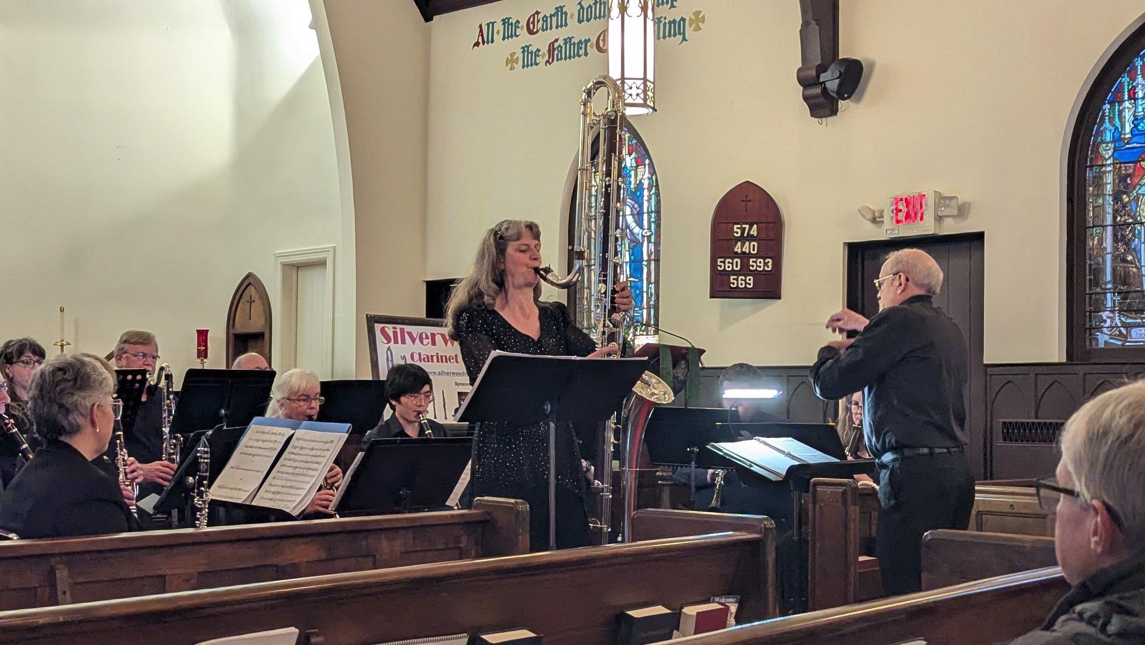 A clarinet choir, with conductor, performing in a church sanctuary; out in front is a soloist playing a contrabass clarinet. Which, if you've never seen one, is gigantic.