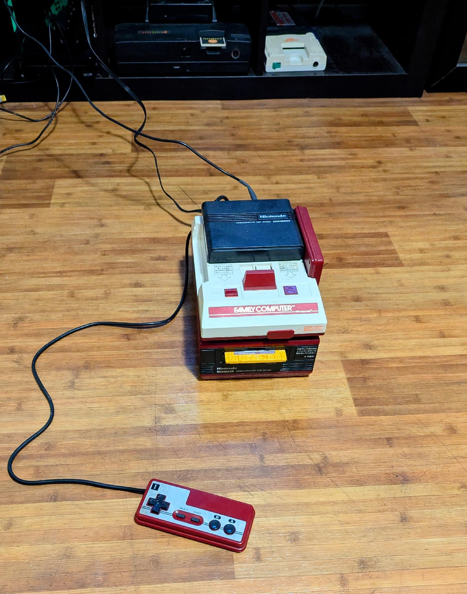 My Famicom Disk System on my floor, controller 1 undocked and pulled foward. A yellow disk protrudes from the disk slot.