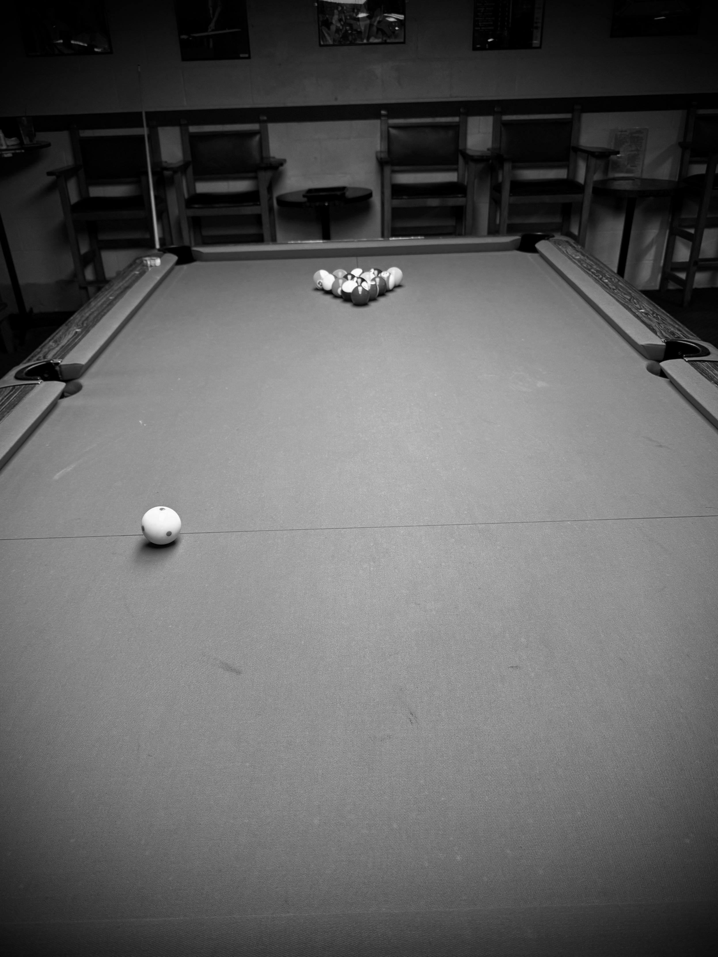Black and white photo of a pool table with the balls racked.