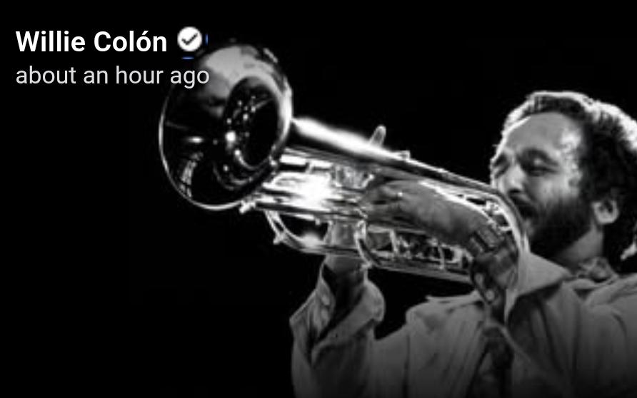 Black and white photo of younger Willie Colon happily playing a trumpet.