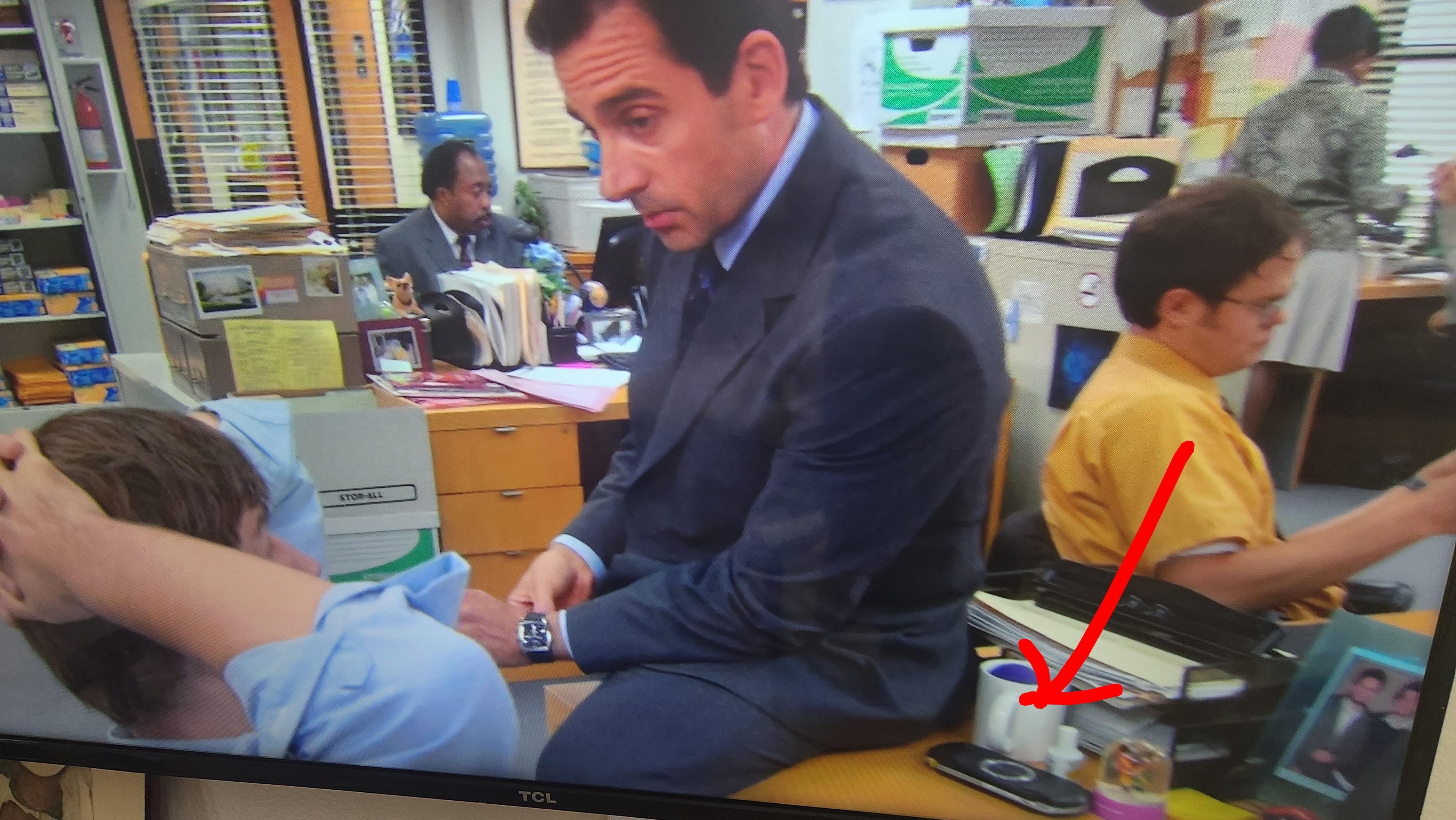 Michael sits on Jim's desk and talks to him. An arrow points to the PSP. S2E06.