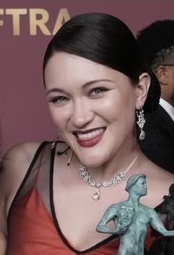 Isa Briones smiling holding her  Actor award. She is wearing a red and black dress and diamond earrings and necklace.