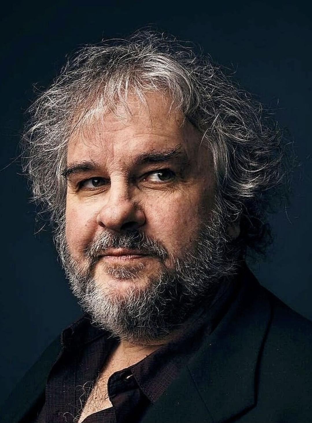 Peter Jackson smiling at the camera. black shirt. a wee bit of chest hair.