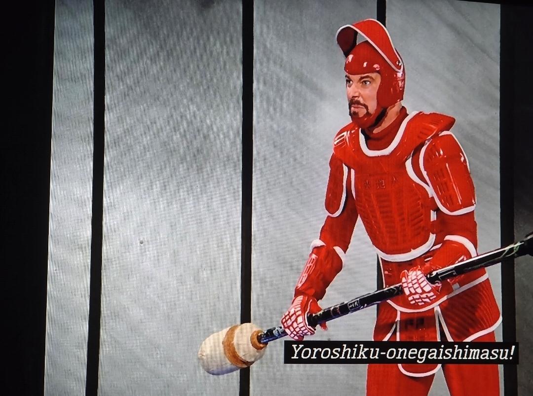Will Riker wearing white and white plastic armor that kind of looks a bit like Shogun armor. But with a helmet whose visor is above his head. He is holding a long stick with a bulbous portion at the end. He looks angry. He's just told his dad that it should've been him (his dad) who died instead of his mother and then he says yoroshiku-onegaishimasu!