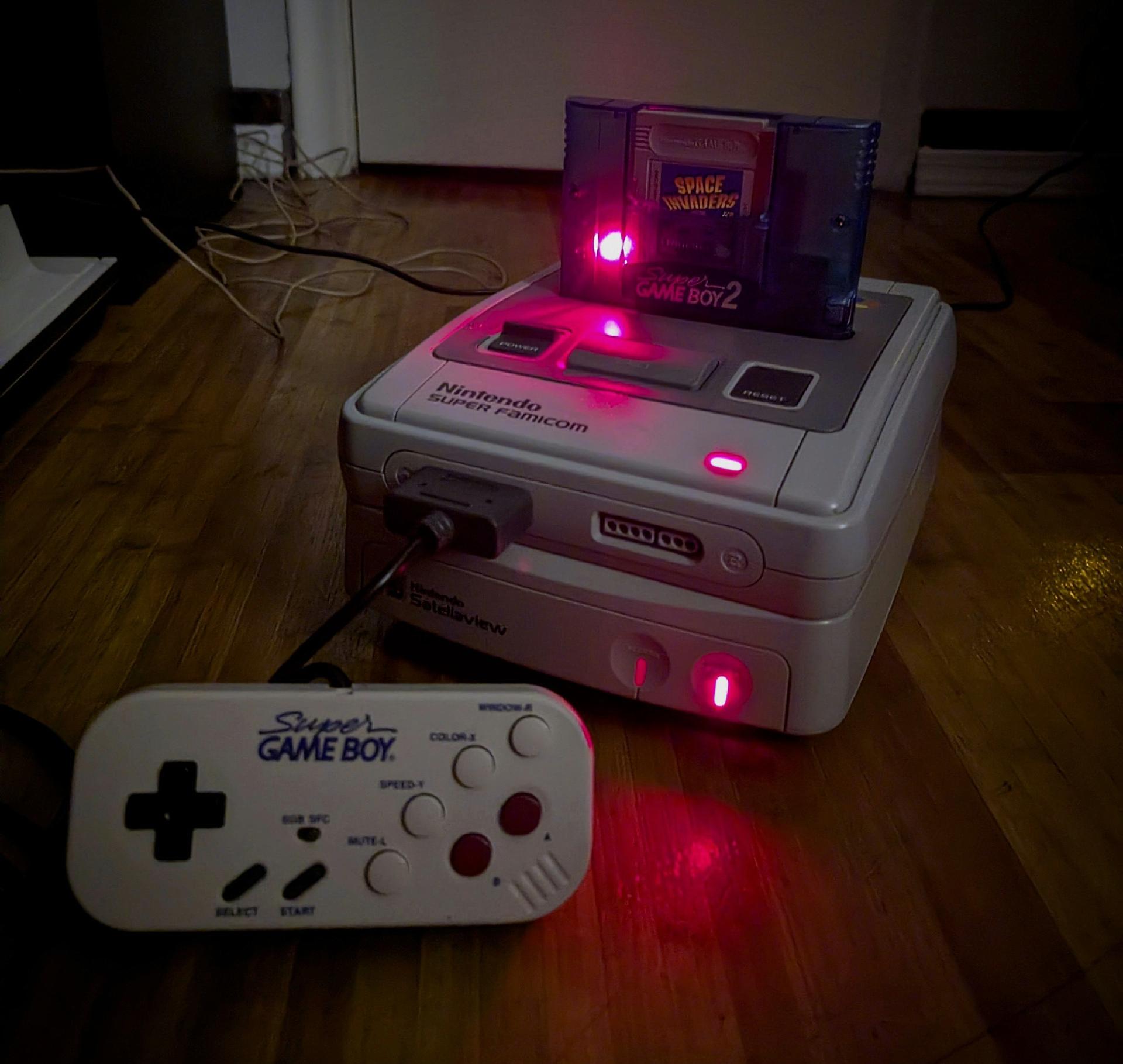 Super Famicom with Broadcast Satellaview and Super Gameboy 2 plus the Hori Super Gameboy Commander in the dark lit up by the 3 red LEDs
