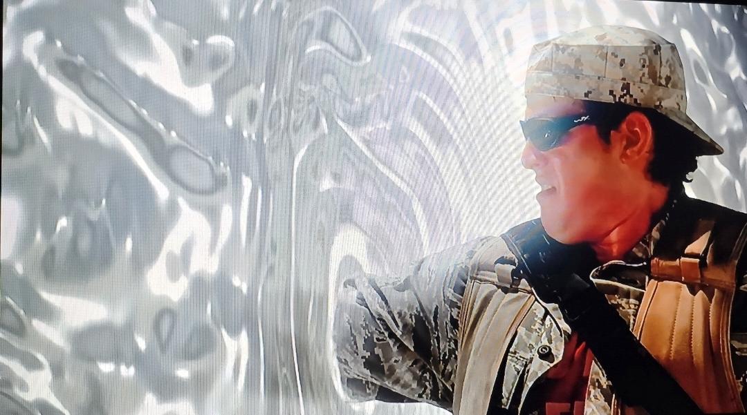 David Blue as Eli heroically holds open the gate by putting his arm in the event horizon. He is wearing deser fatigues and cap in backwards. He's sunburned, sweating and wearing sunglasses.