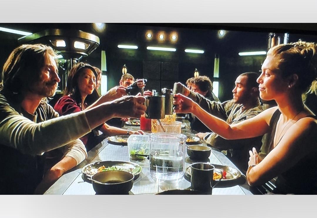 The cast of Stargate Universe are making a toast around the table before going into suspended animation for 3 years.