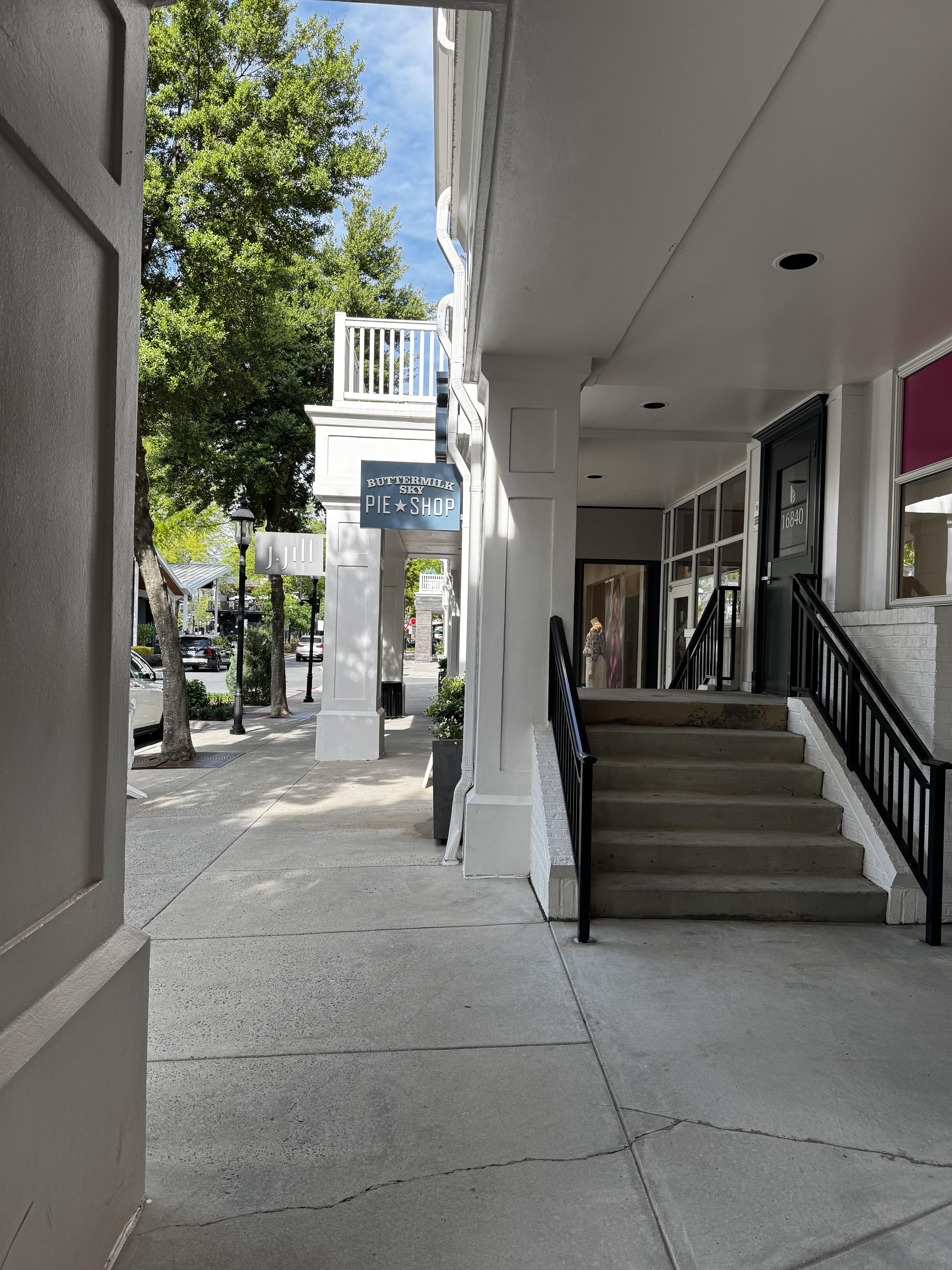 A bright street with white-painted wooden trimmed buildings has a leafed out green tree and a blue sky.  A baby blue sign for "Buttermilk Sky Pie Shop" hangs in the center of the photo.  Pretty good small pies.  I mean, not that I would know.