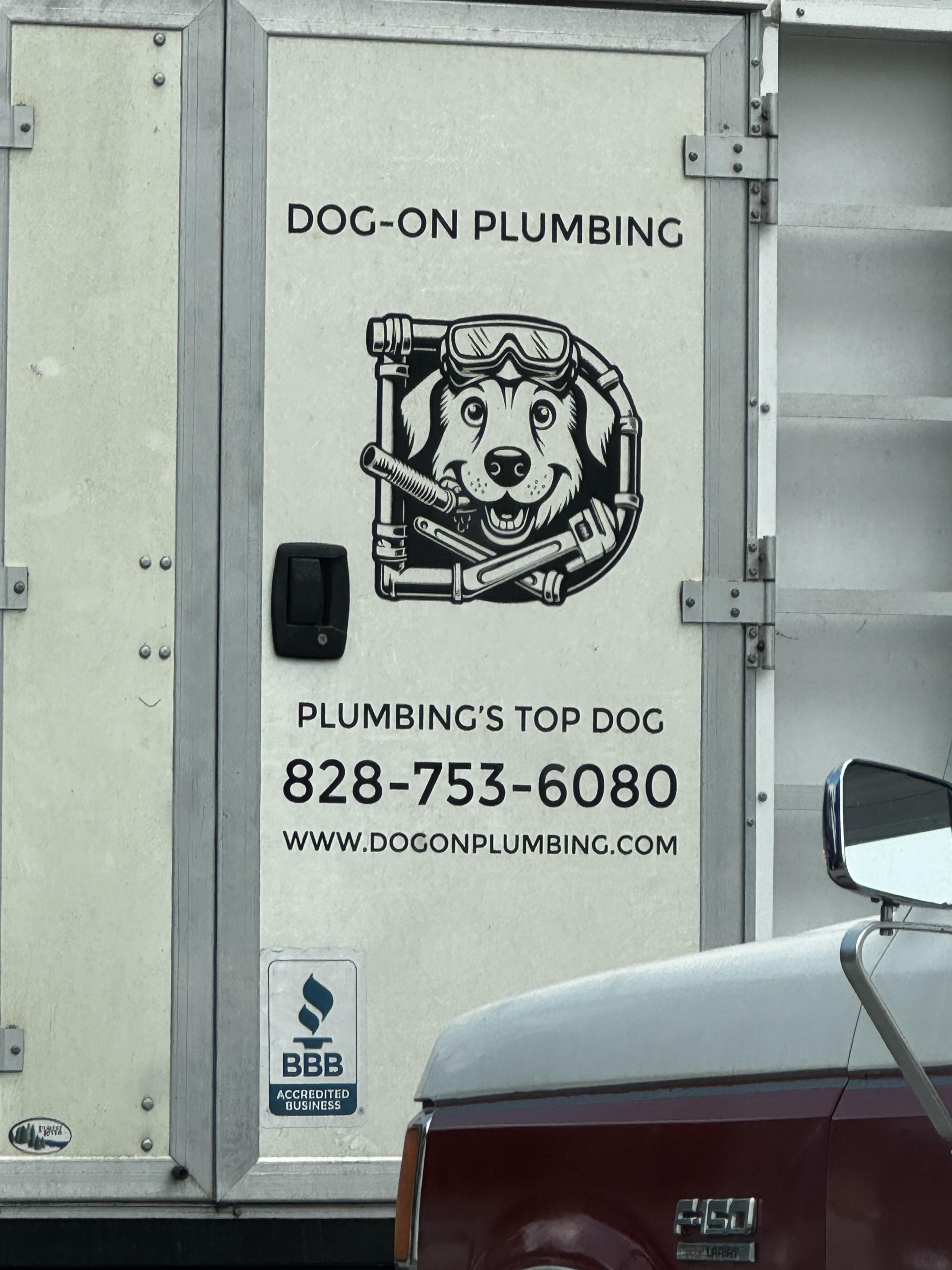 A white plumbing van has a black logo on it with a smiling dog (Golden?) holding a series of pipes and tools. The name is dog-on plumbing.