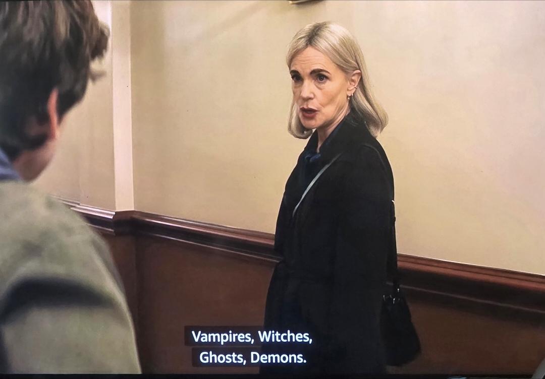 In the hallway of the Dakota in NYC, Maureen McGovern, in a dark suit and a blonde bob, tells Guy in a khaki jacket, "Vampires, Witches, Ghosts, Demons."