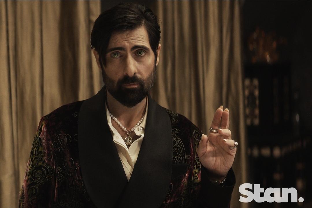 Jason Schwartzman as Aburron , a Vampire. He's dressed in a crushed velvet dinner jacket and wearing a pearl necklace with a silver amulet. His beard and mustache and VERY black and immaculately trimmed. His left hand is raised with index and middle finger straight. He is wearing rings on almost every finger. His fingernails are long but unpainted. His expression is one of patient long suffering. Behind him are gold curtains and a library with expensive antique books.