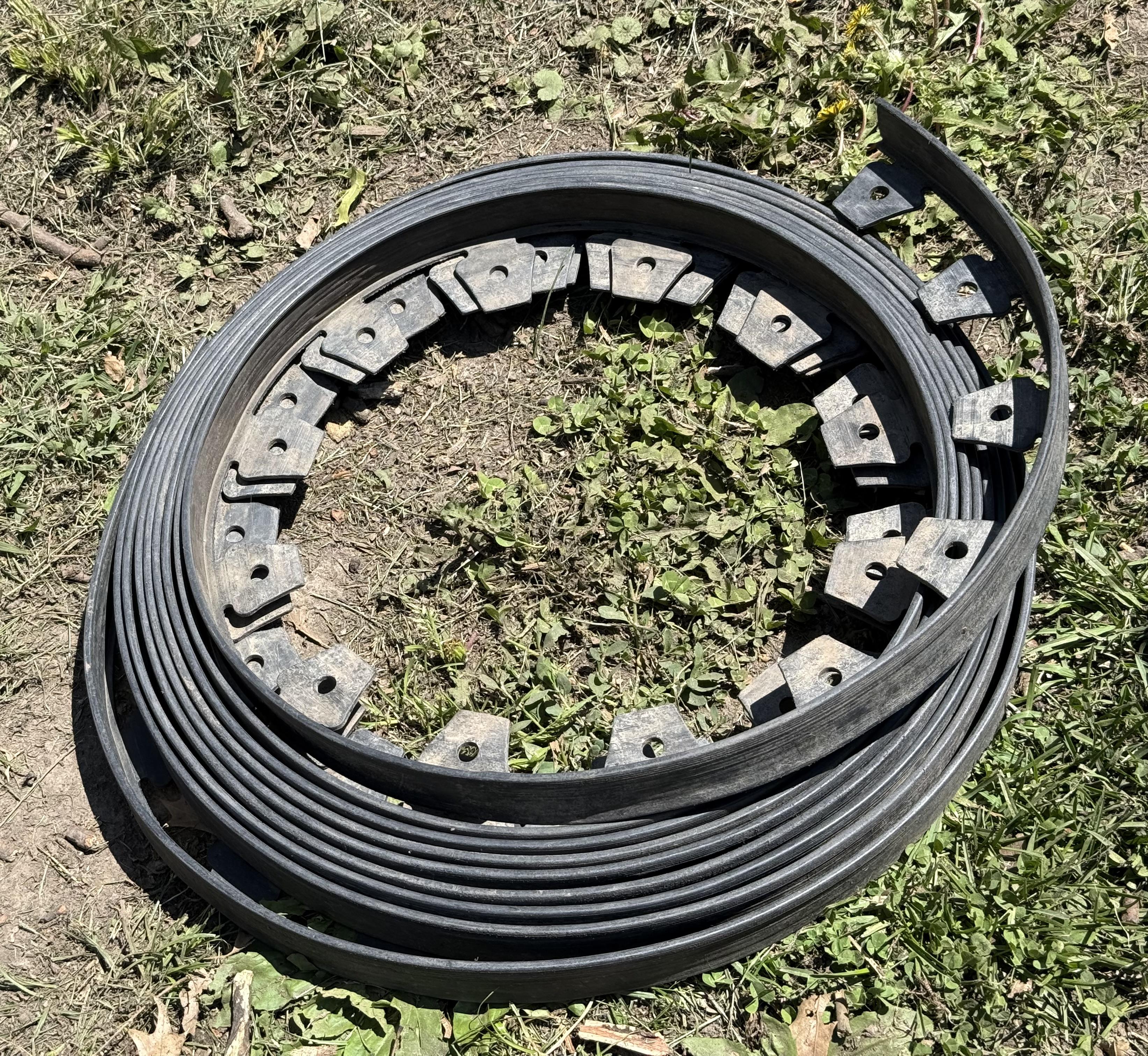 A coil of cheap black plastic edging tightly rolled. It’s faded and dirty from its time in the river. The coil lays on a sad bit of patchy lawn