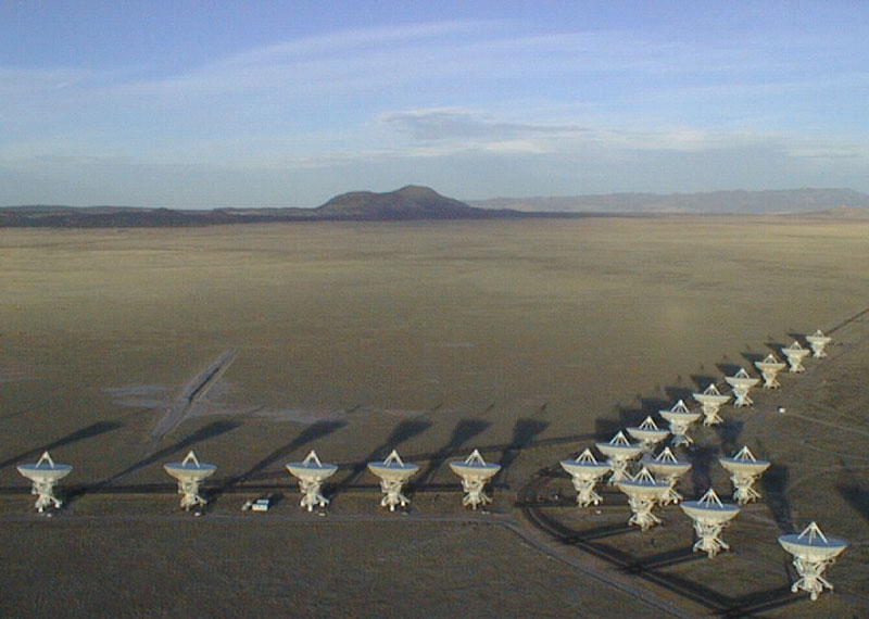 Nineteen radio telescopes arranged in a Y formation on an otherwise mostly featureless plain with mountains in the distance.