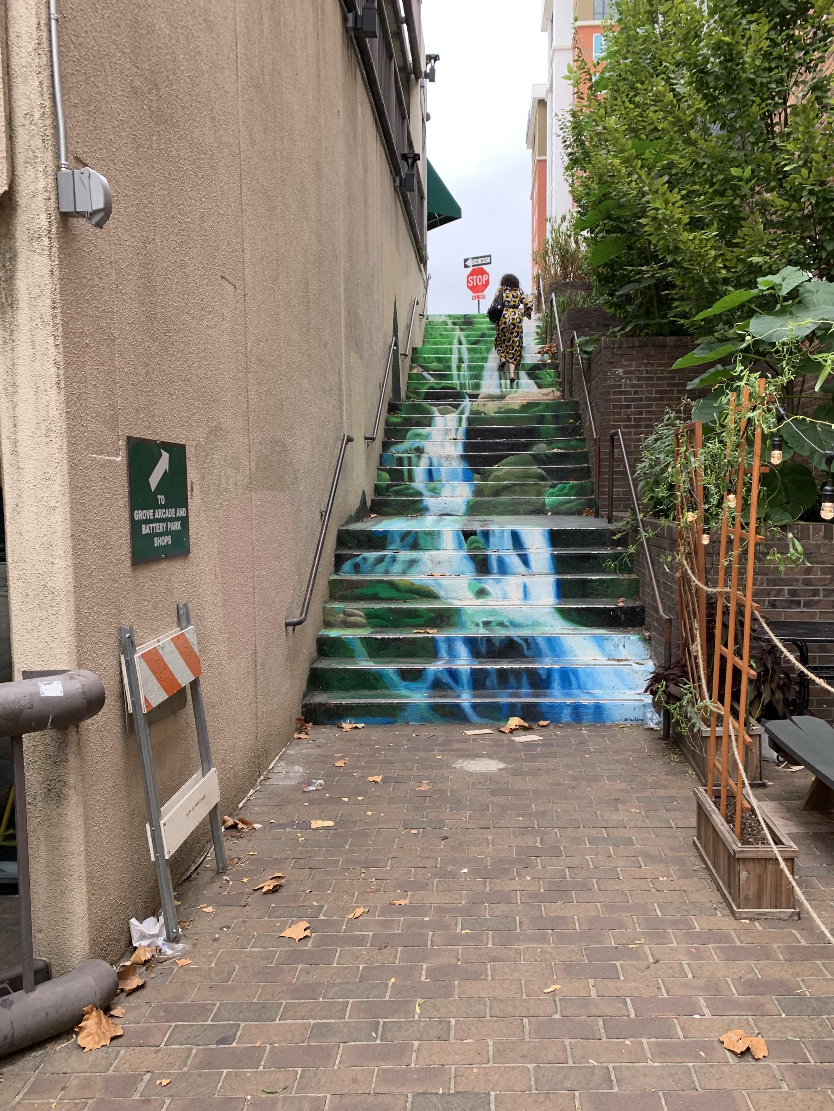 A cascading set of 5 concrete stairways have been painted so that the risers look like a waterfall, something that my area of North Carolina is well-known for.  It is a narrow alley which connects Wall St with Battery Park Ave, and was intended to encourage people to visit the shops on each street.  

In the photo a person in a leopard-like print dress and high heels is most of the way up the staircase on the right.  A stop sign is visible near the top of the stairs, and a small trellis flanks the bottom area on the right, appearing to section off an outdoor eatery, perhaps.