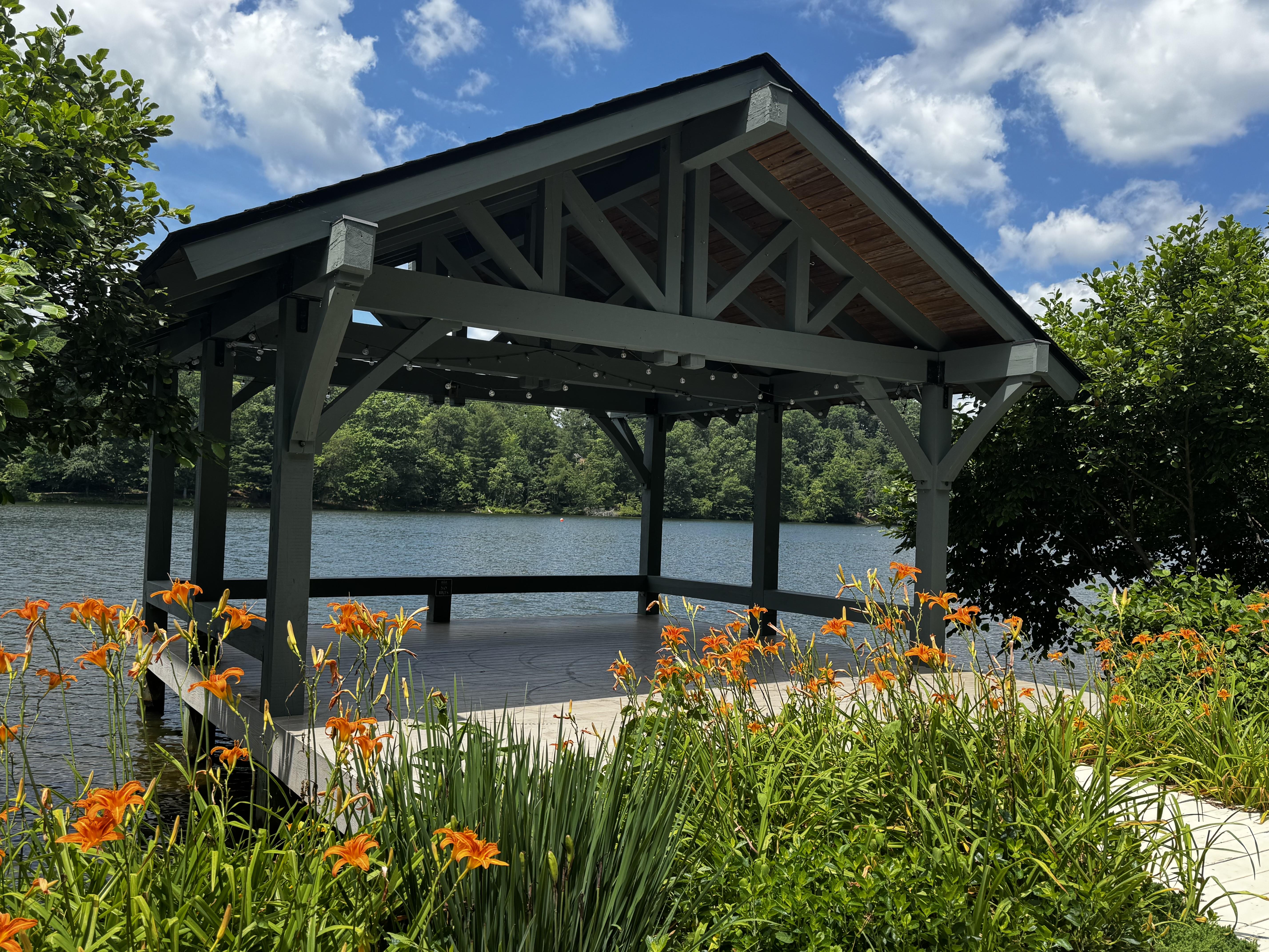 A covered pavilion overlooking a largish lake on a very sunny, warm day.  The entrance to the covered space is flanked by beds of orange day lilies, and makes an attractive sight.

There are not benches or seats inside the pavilion, which  might lead someone to wonder why it is there.  Looking carefully in the water behind, you might be able to pick out a few small heads.  Eeek.
