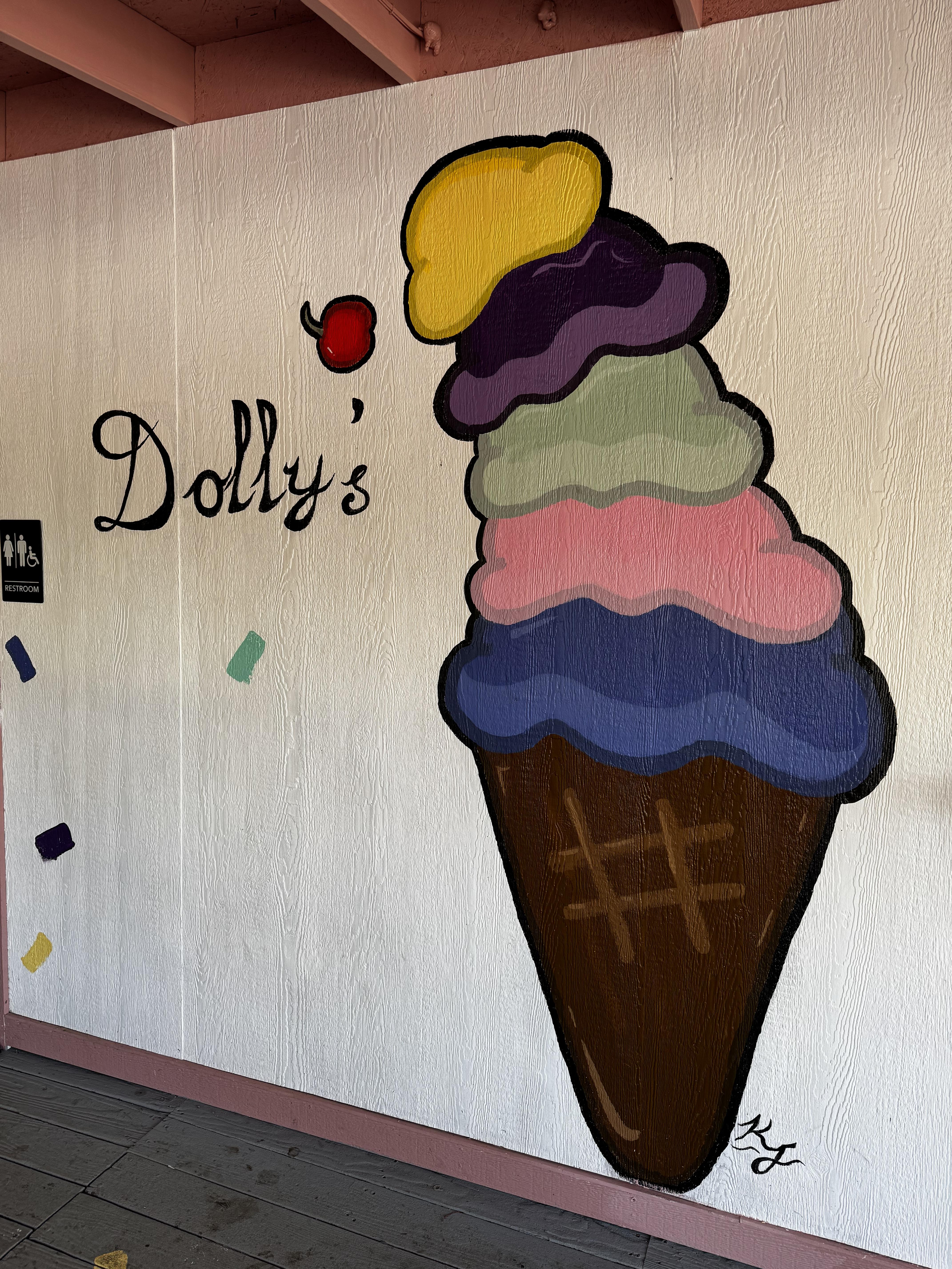 A mural on the outside of the porch shows a cone with 5 different-colored scoops of ice cream and a cherry losing the battle with gravity, next to the name "Dolly's" in black script.   Brightly colored, and quite large.